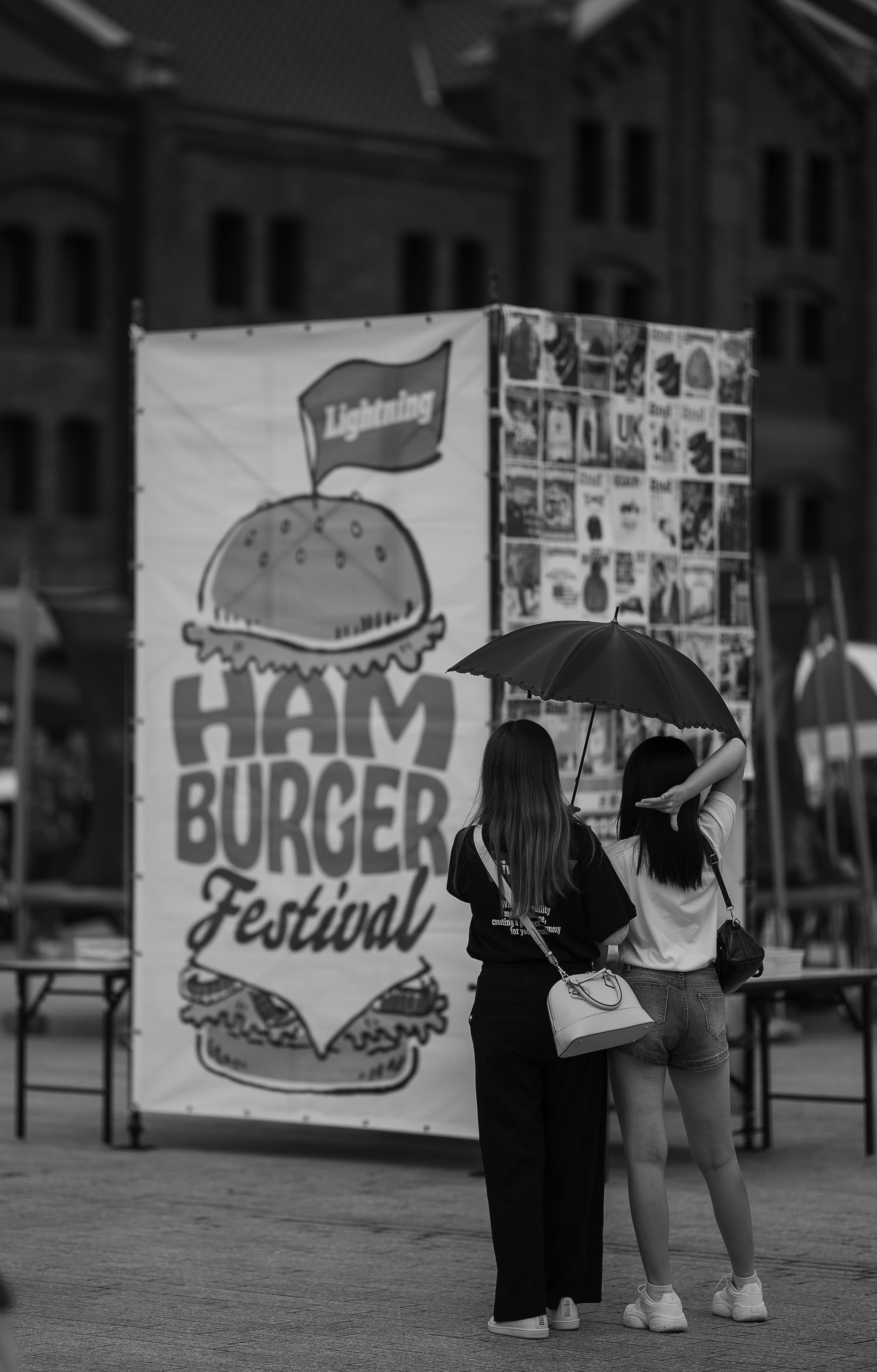 Two women under umbrella near hamburger festival banner