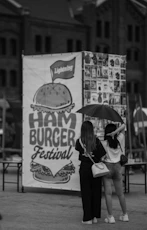 Two women under umbrella near hamburger festival banner