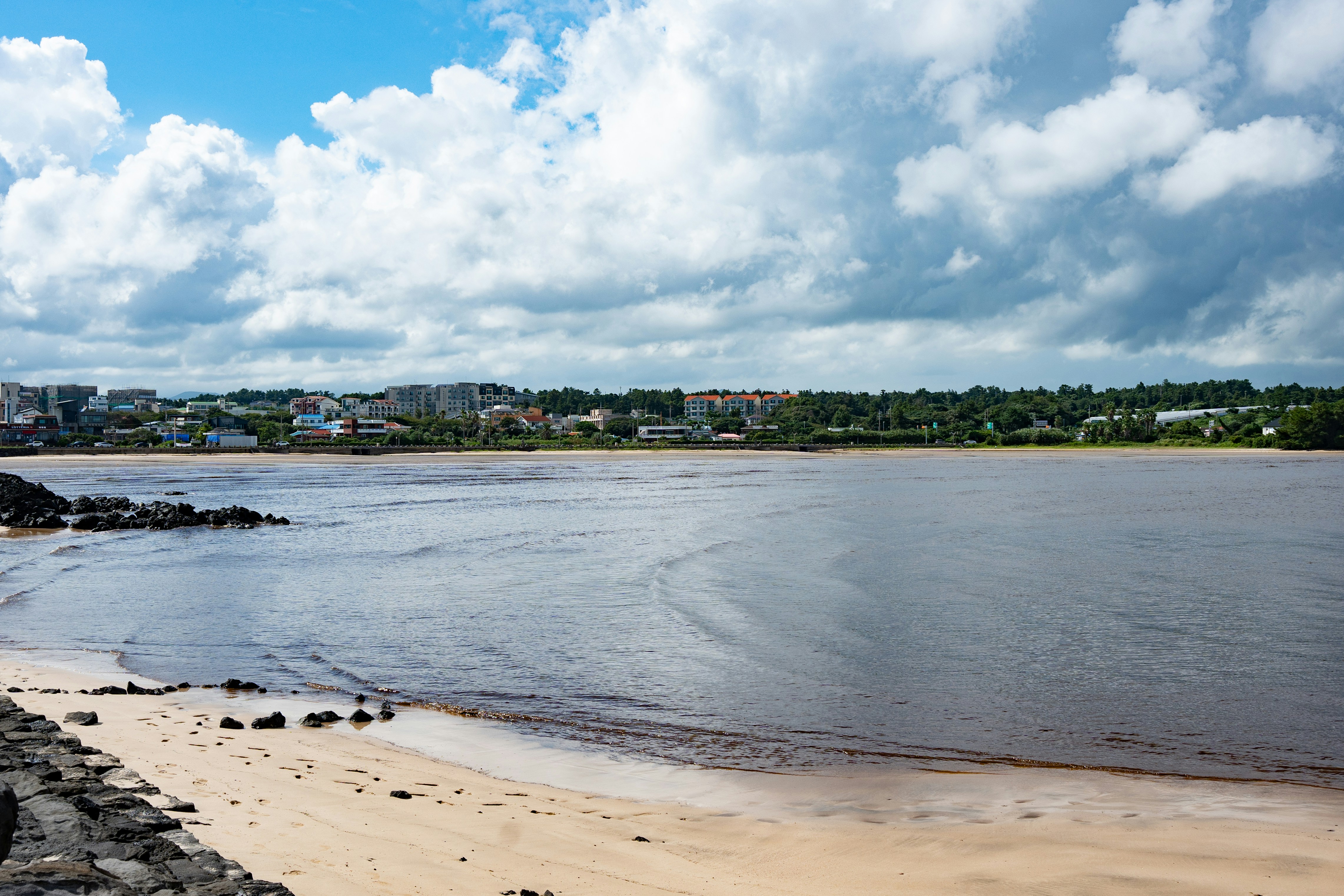 Beach with calm water and distant town under clouds
