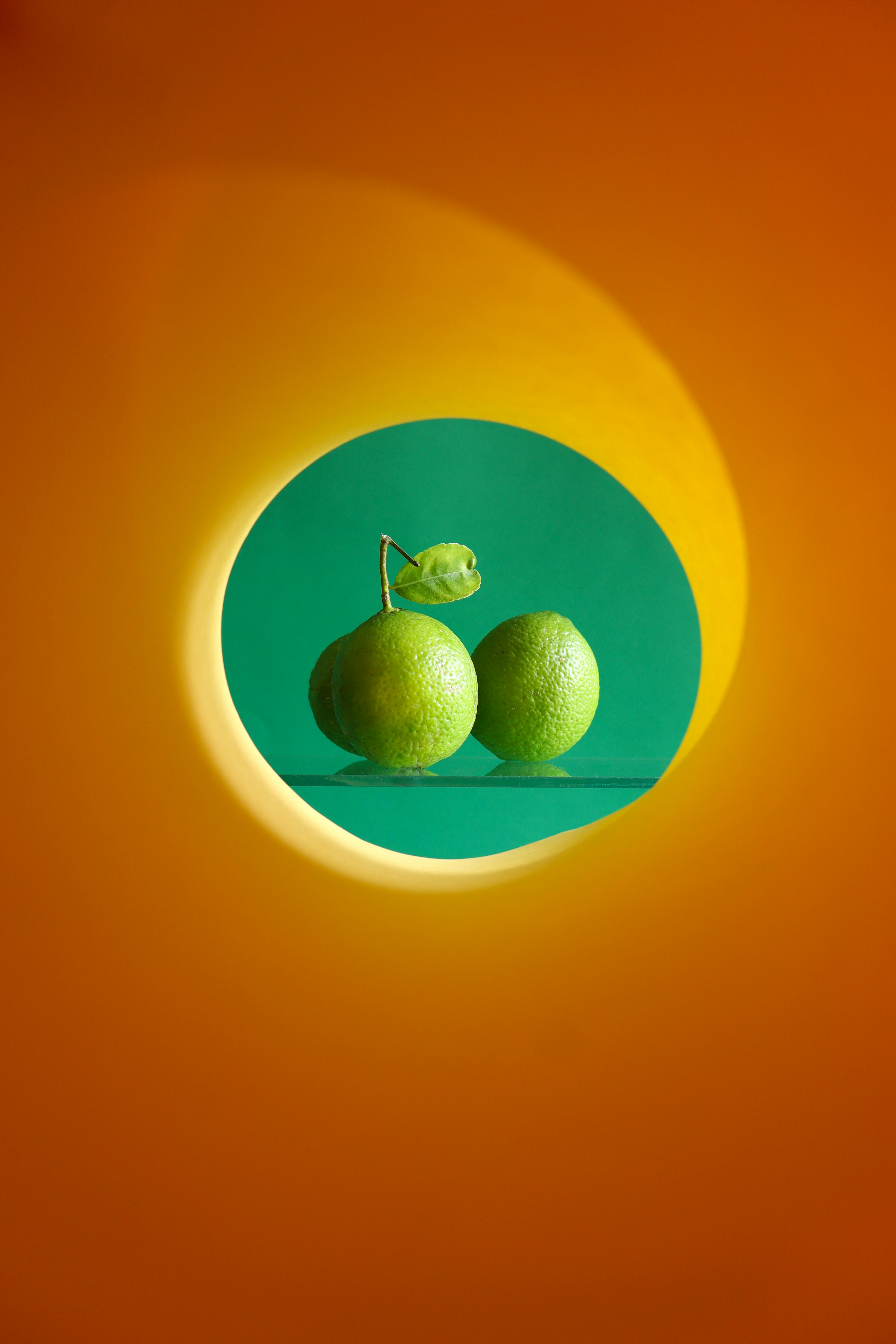 Two green limes on a green surface.
