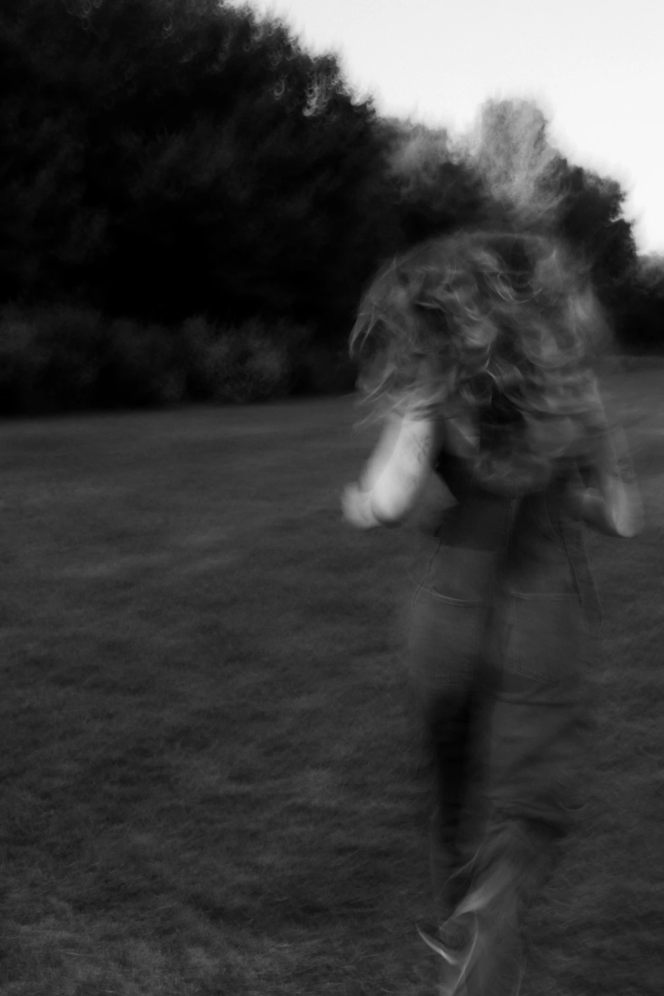 Person running on grassy field with blurred motion, wearing black clothing in background