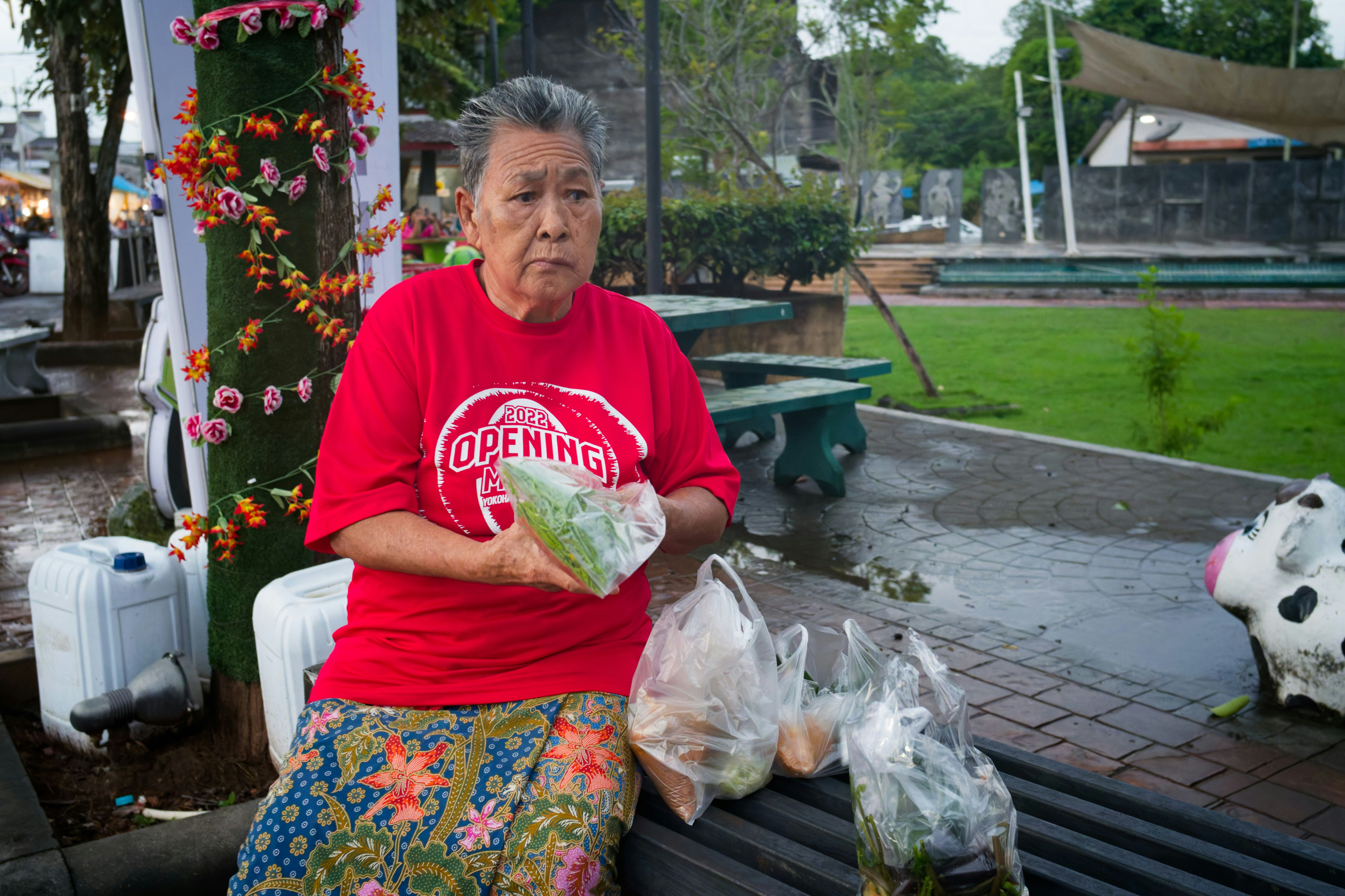 Elderly woman in red shirt holding produce.