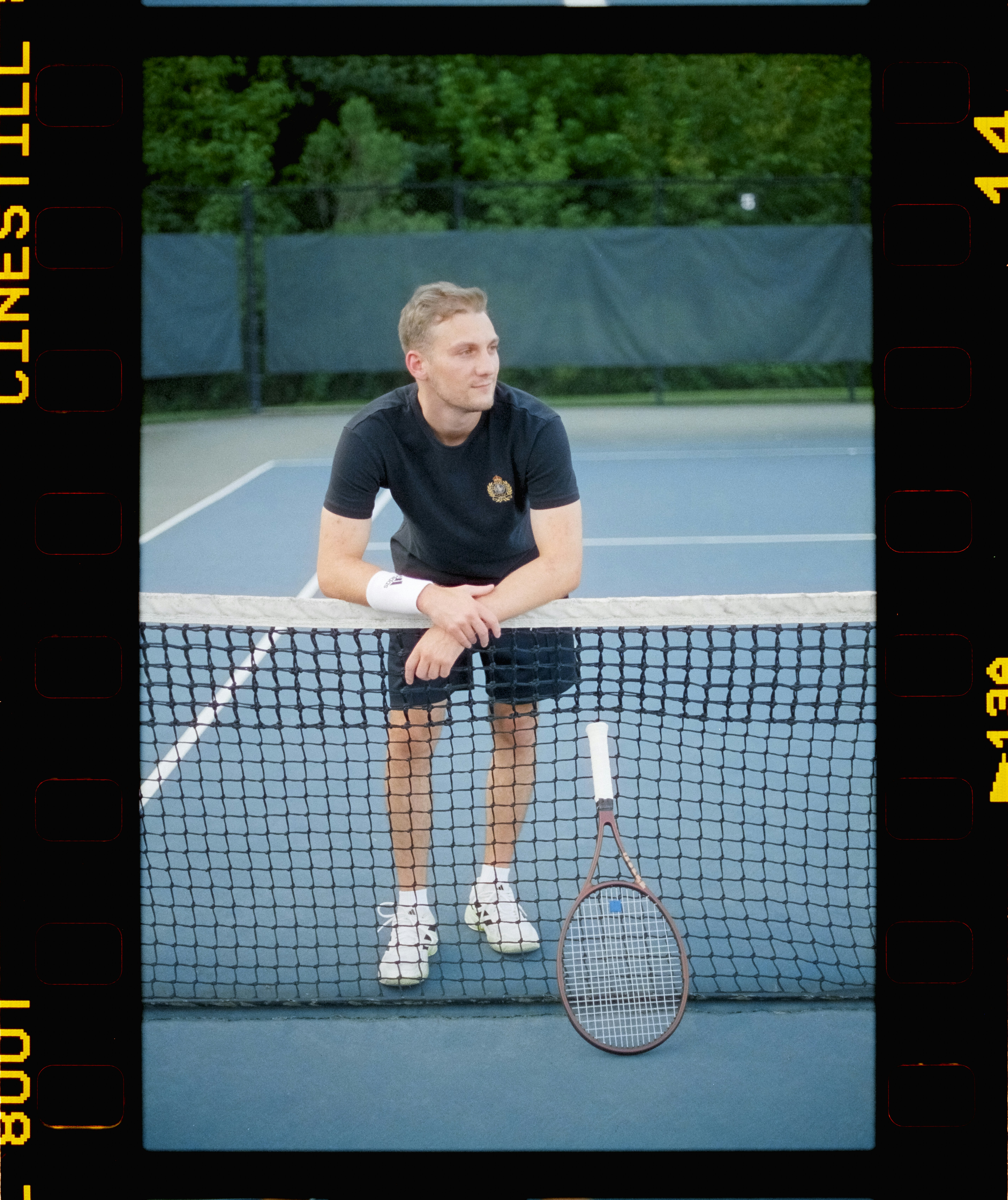 Man in tennis attire leaning on net with racket.