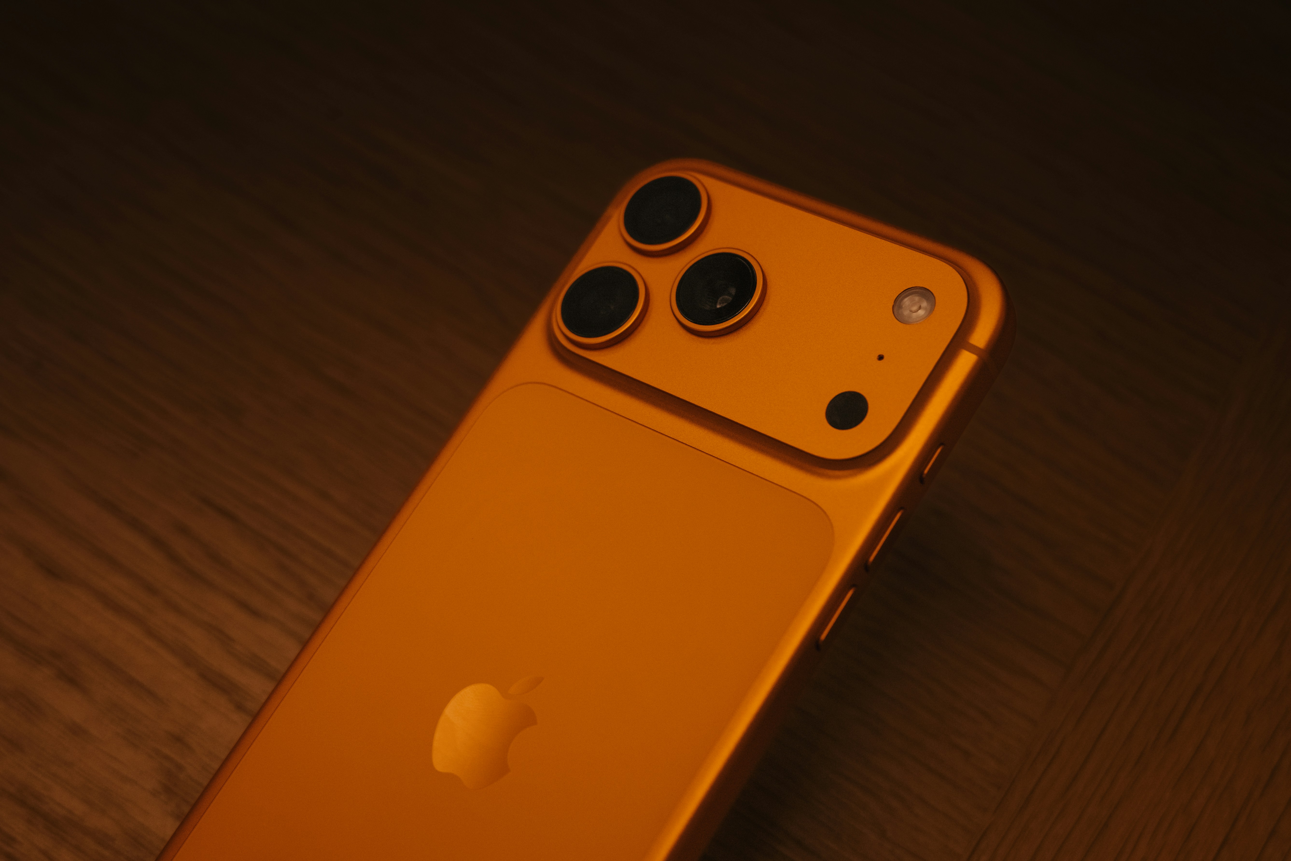 iPhone 17 Pro Max in orange, with a triple-lens camera shot in warm lighting, has a sleek, premium look.