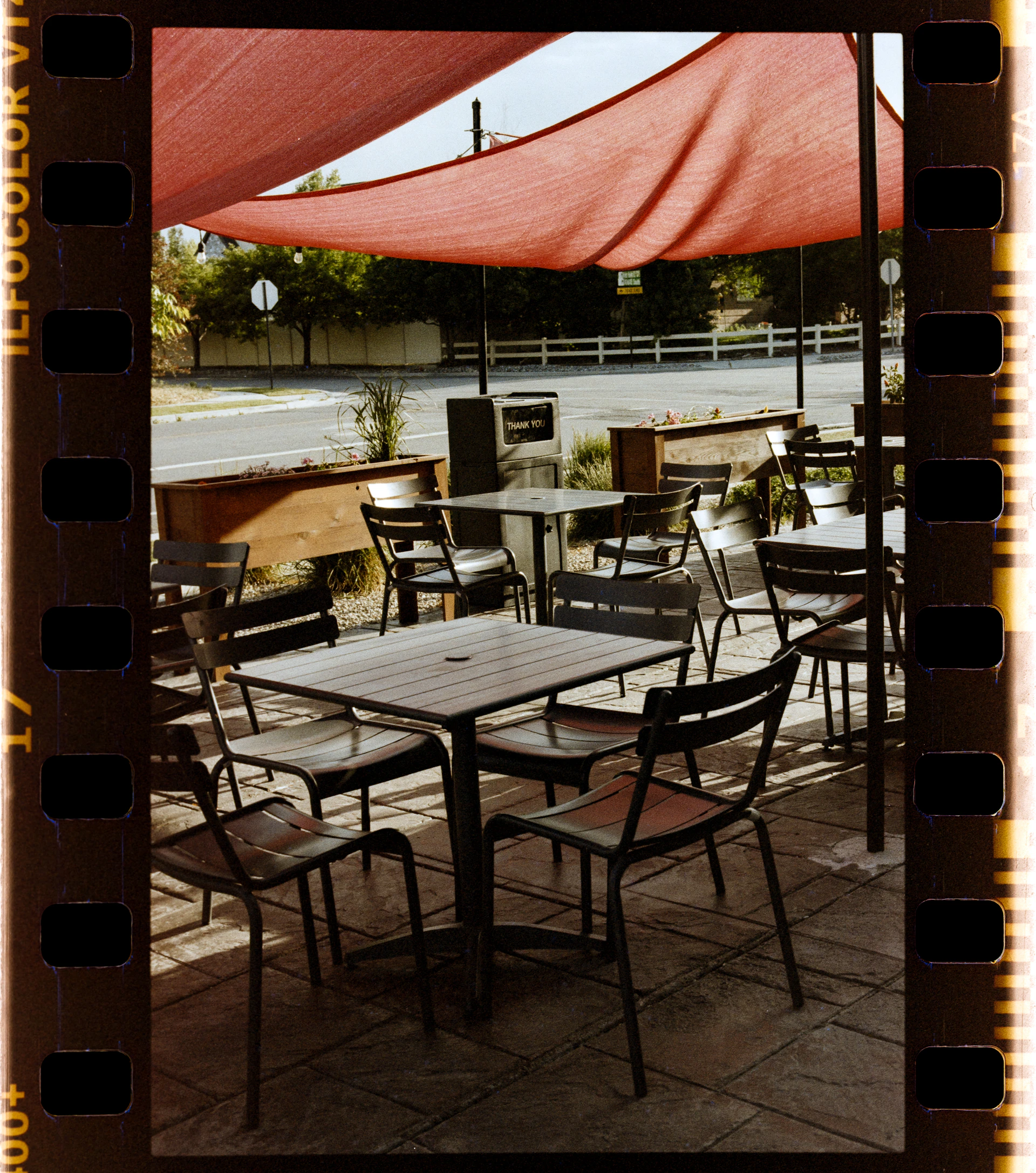 Outdoor cafe tables and chairs under a red awning.