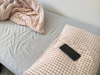A smartphone rests on a checkered pillow on a bed.