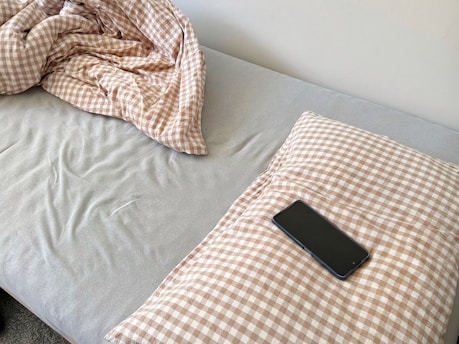 A smartphone rests on a checkered pillow on a bed.