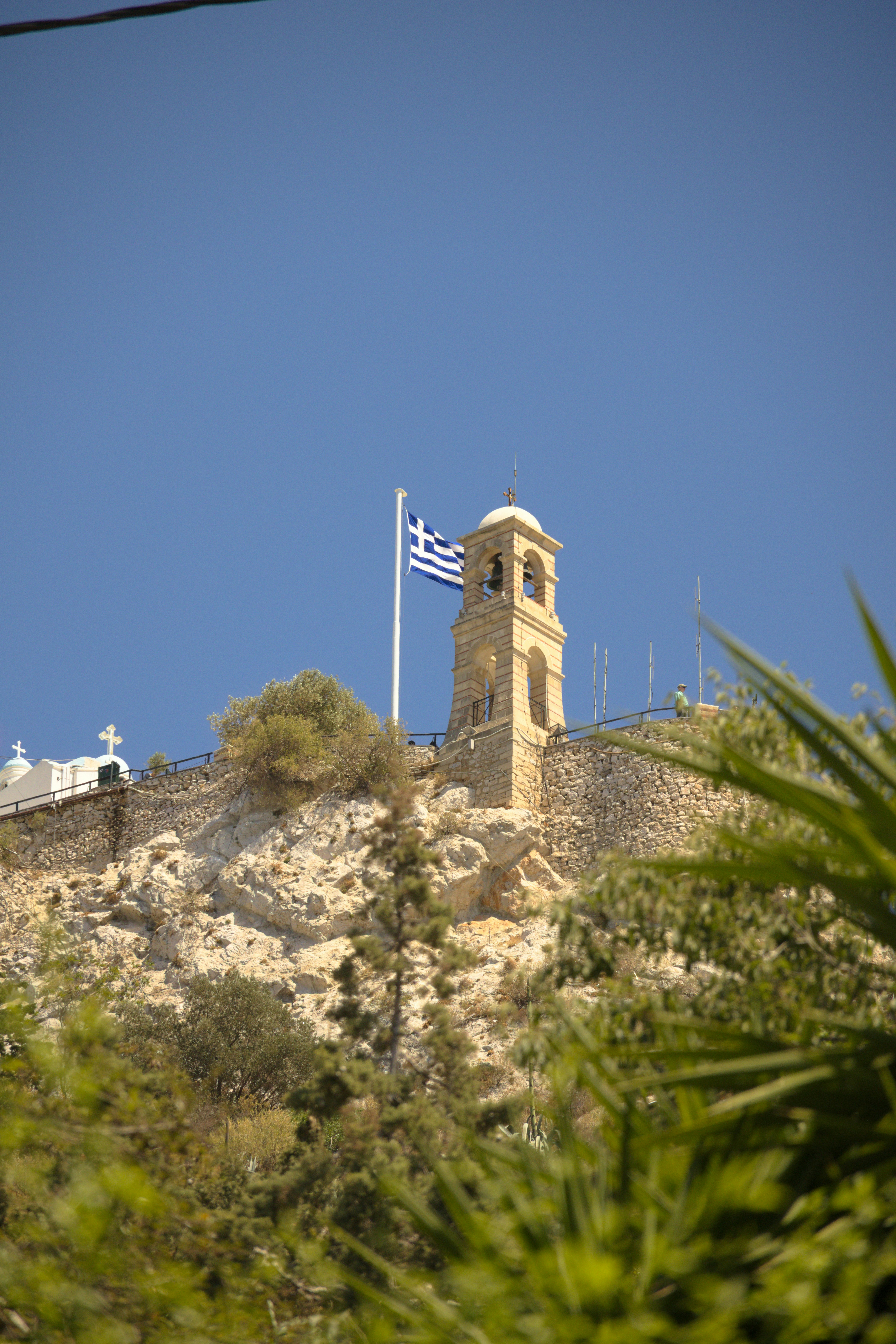Torre sineira com bandeira grega no topo da colina rochosa