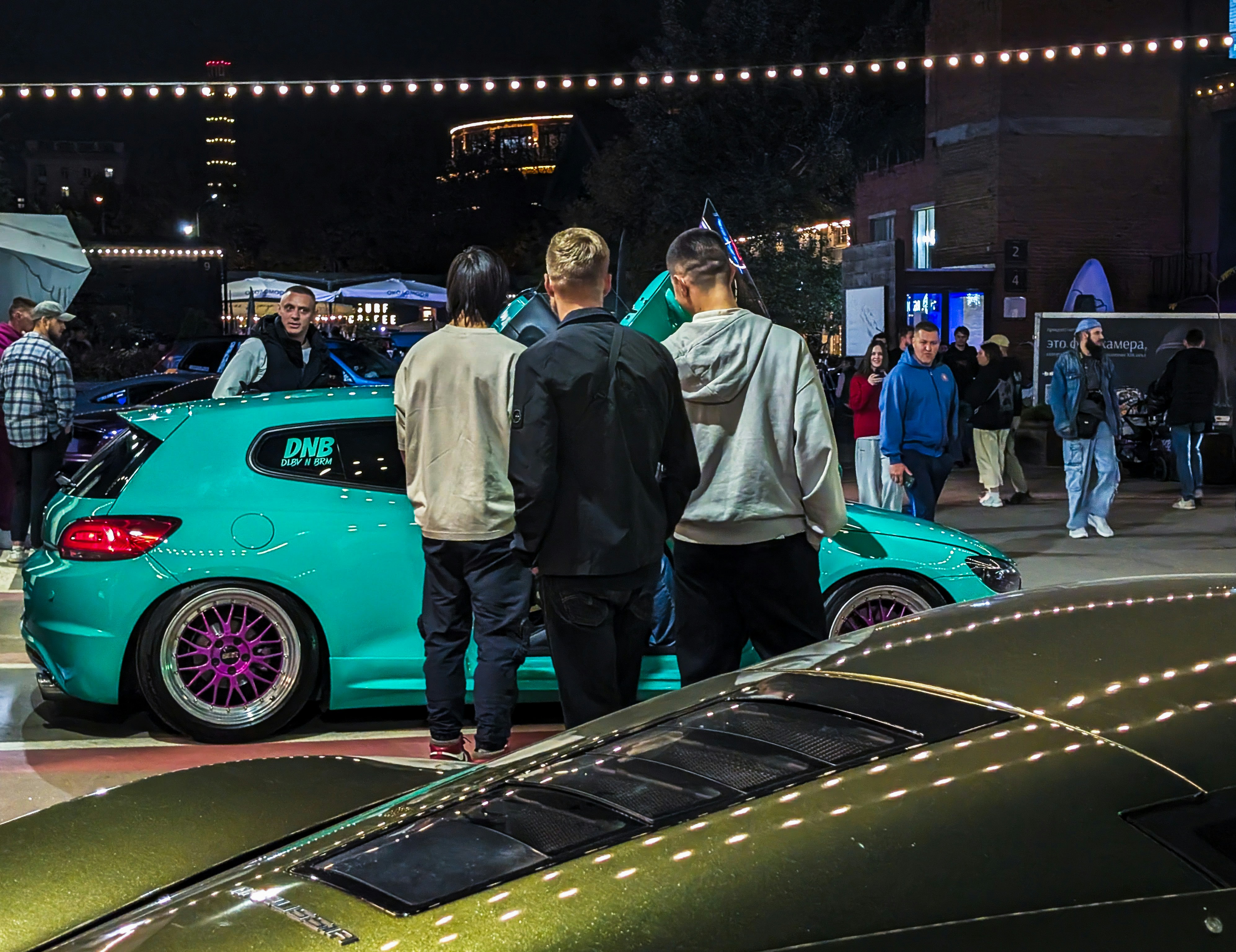 Die Menschen versammelten sich nachts um ein blaugrünes Custom-Auto.