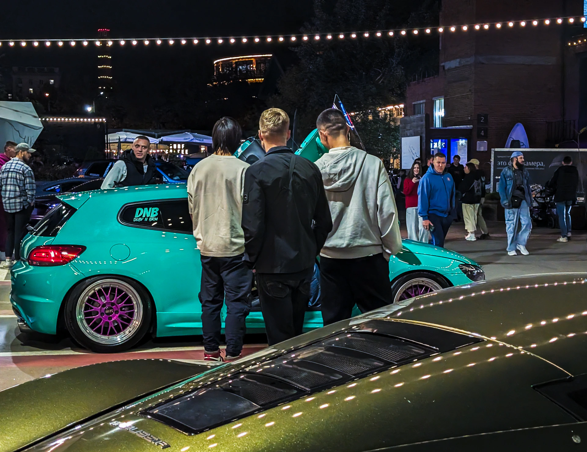 People gathered around a teal custom car at night.