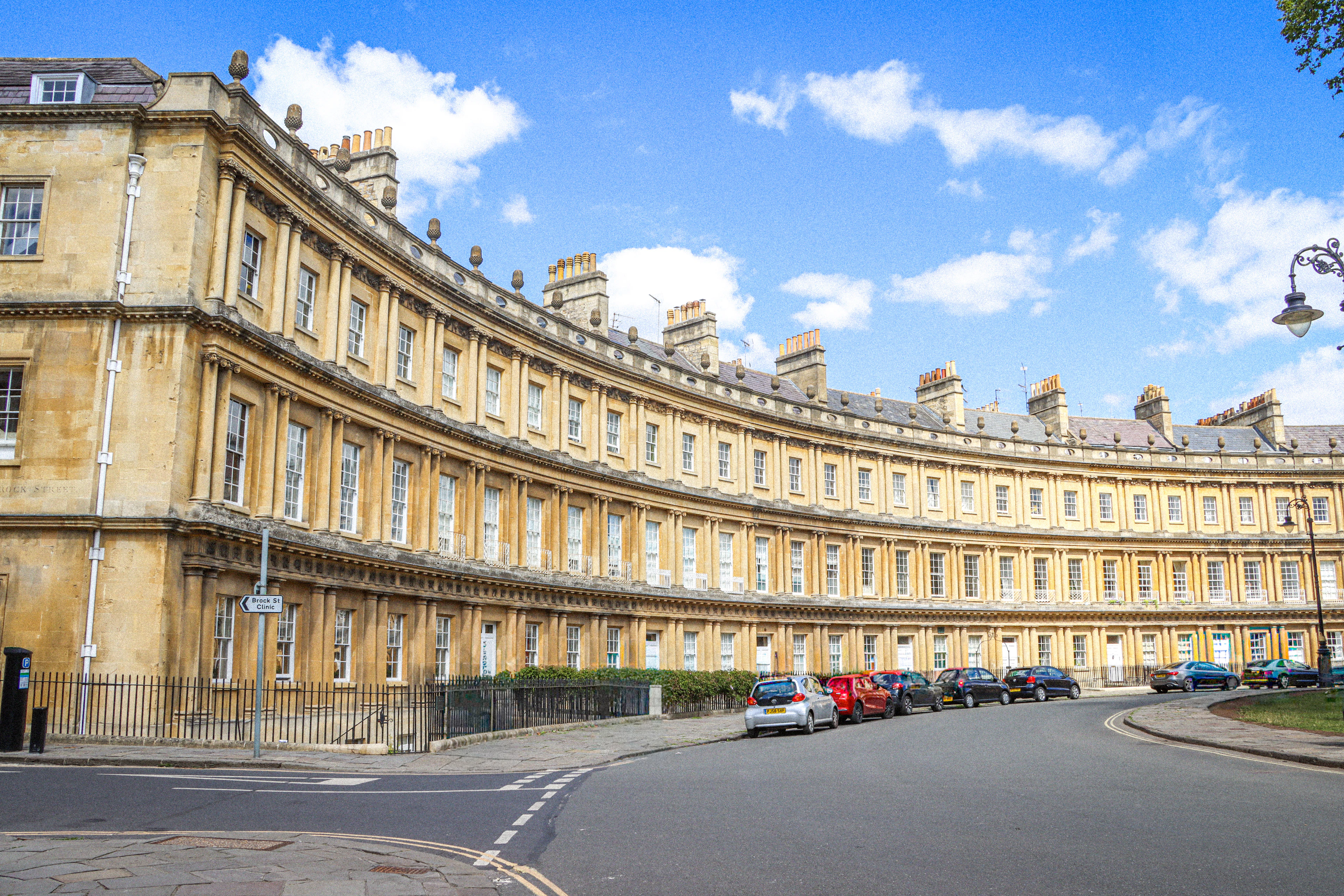 The Circus in Bath, a sweeping curve of honey-coloured Georgian terraces with three tiers of columns and rows of chimneys, under a blue sky scattered with white cloud