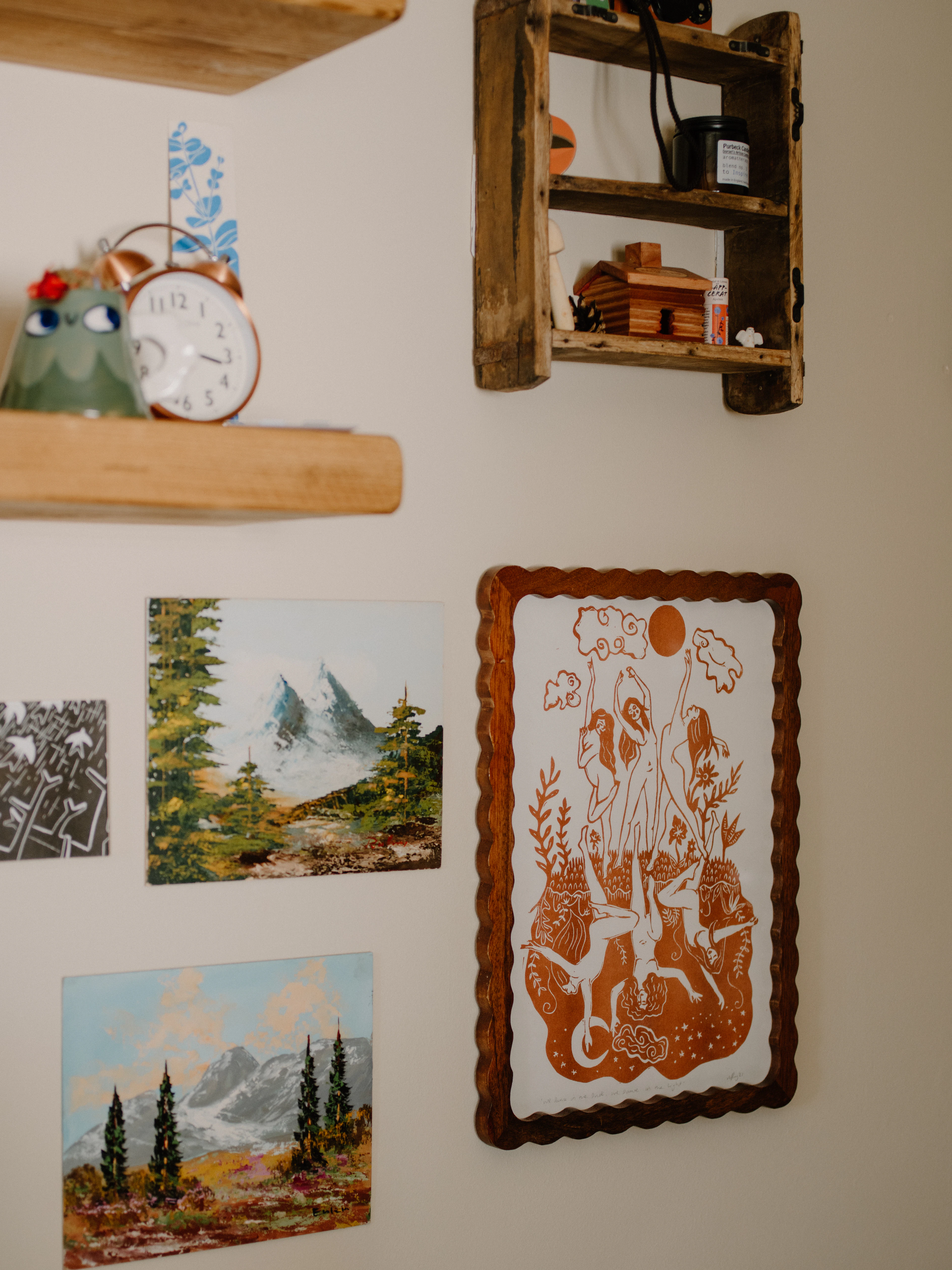 Paintings and a framed illustration hung together on a wall at home.