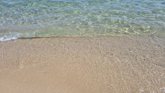 Clear ocean water washes onto a sandy beach shore.