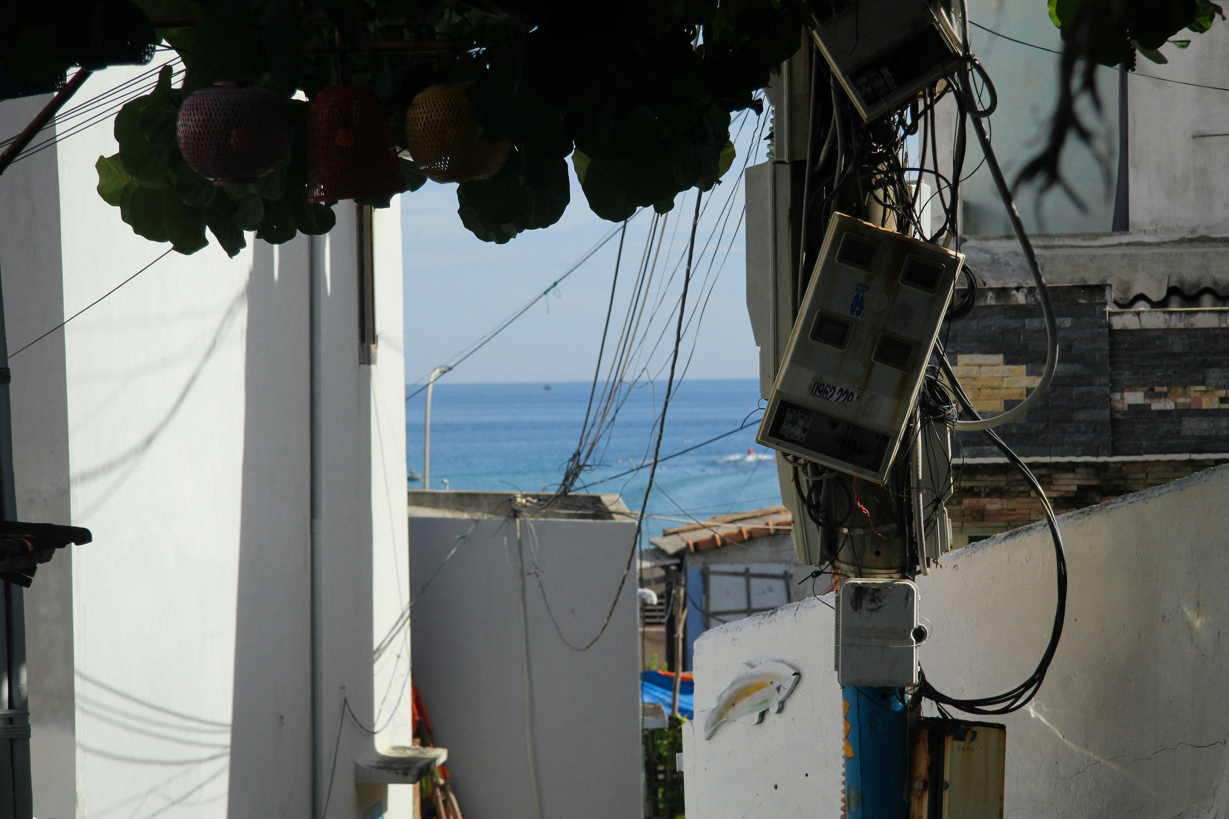 View of the ocean between buildings with tangled wires.