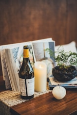 Wine bottle, candle, book, and plant on table.