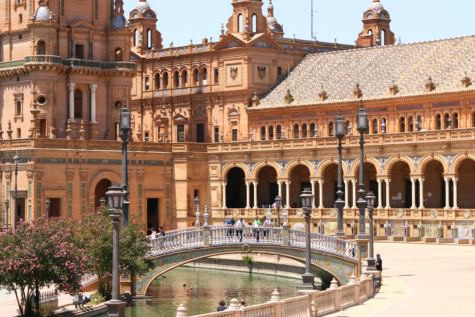 A tiled bridge arching over the canal in front of the brick-and-ceramic palace of Seville's Plaza de España