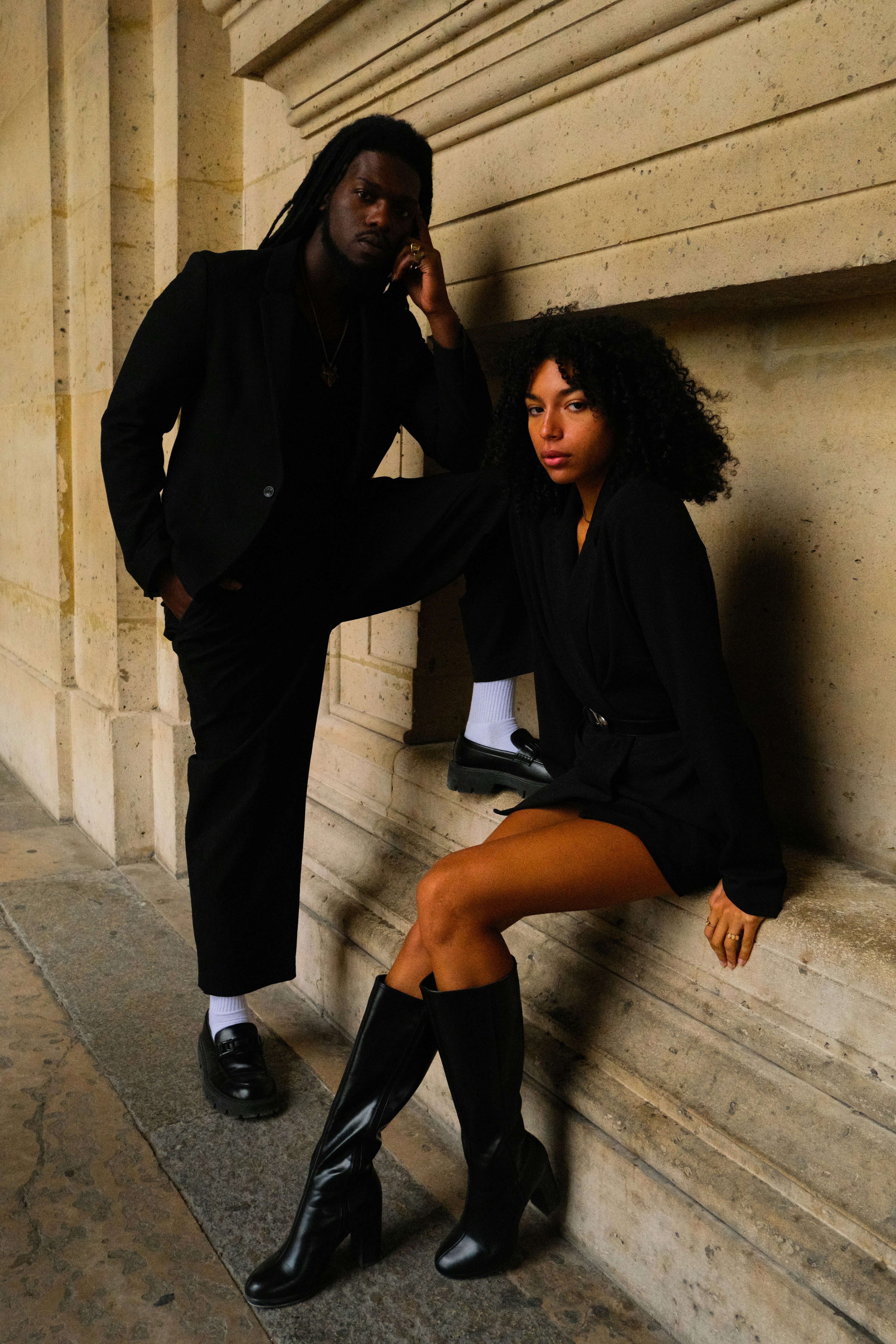 A stylish couple posing in black outfits outdoors.