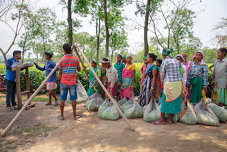 People gathered with large bags of produce near trees