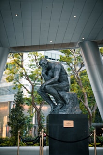 The thinker statue sits on a pedestal outdoors.