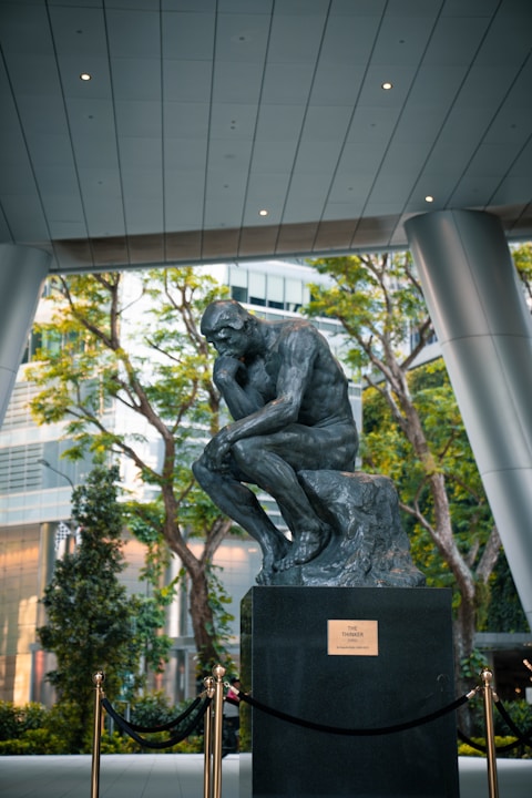 The thinker statue sits on a pedestal outdoors.
