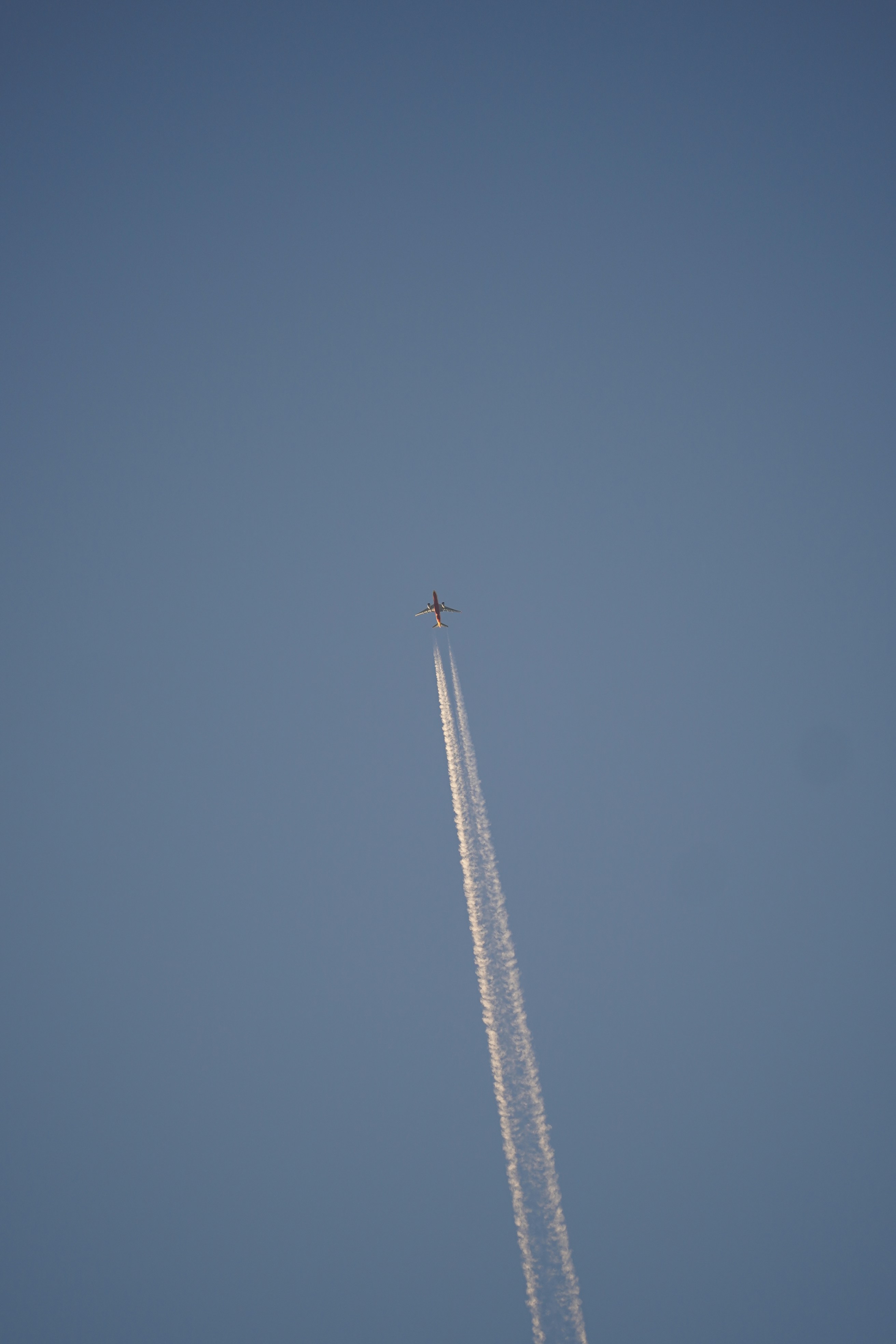 Airplane leaving a contrail across clear blue sky.