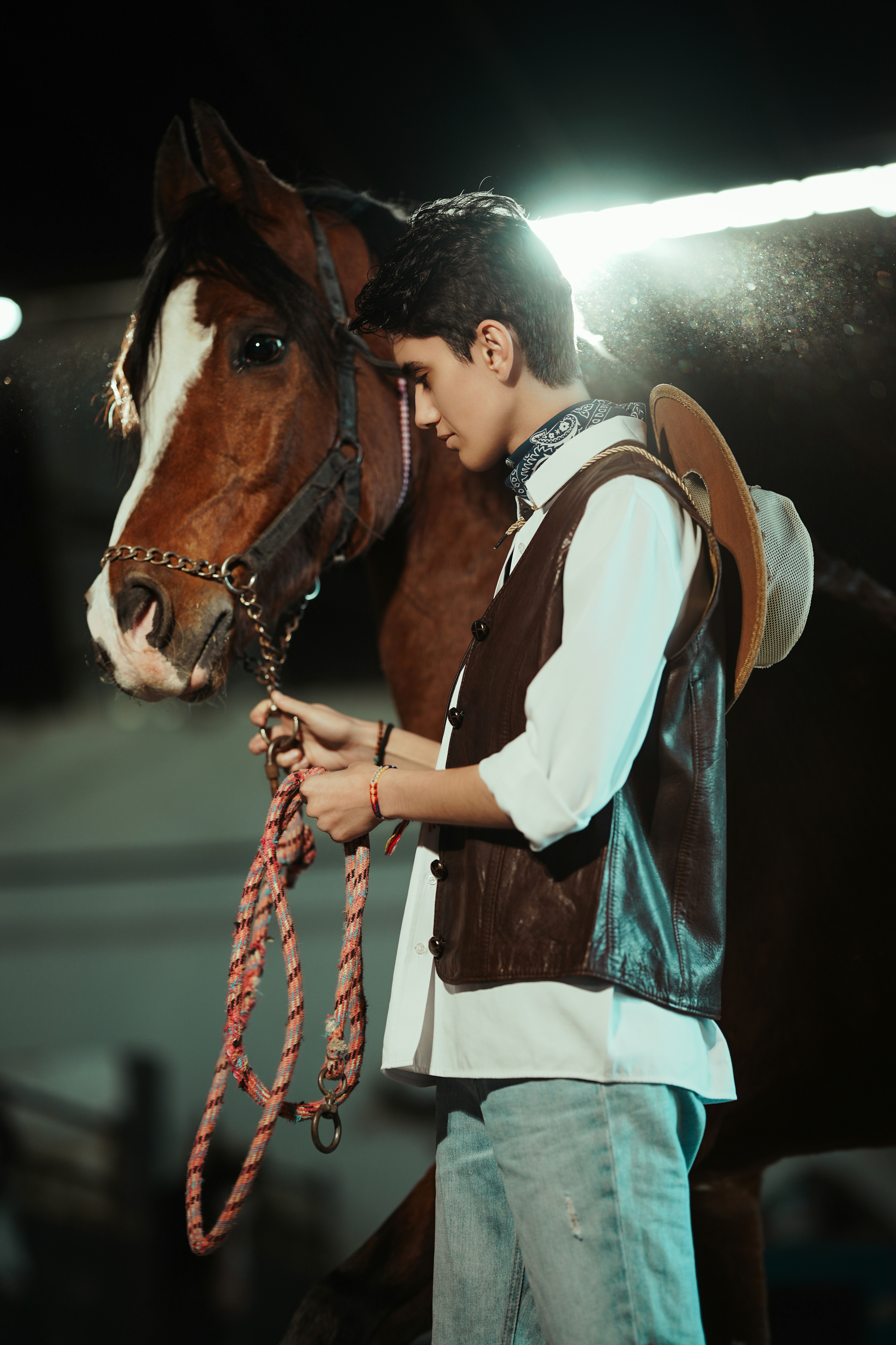 Young cowboy with horse in stable at night