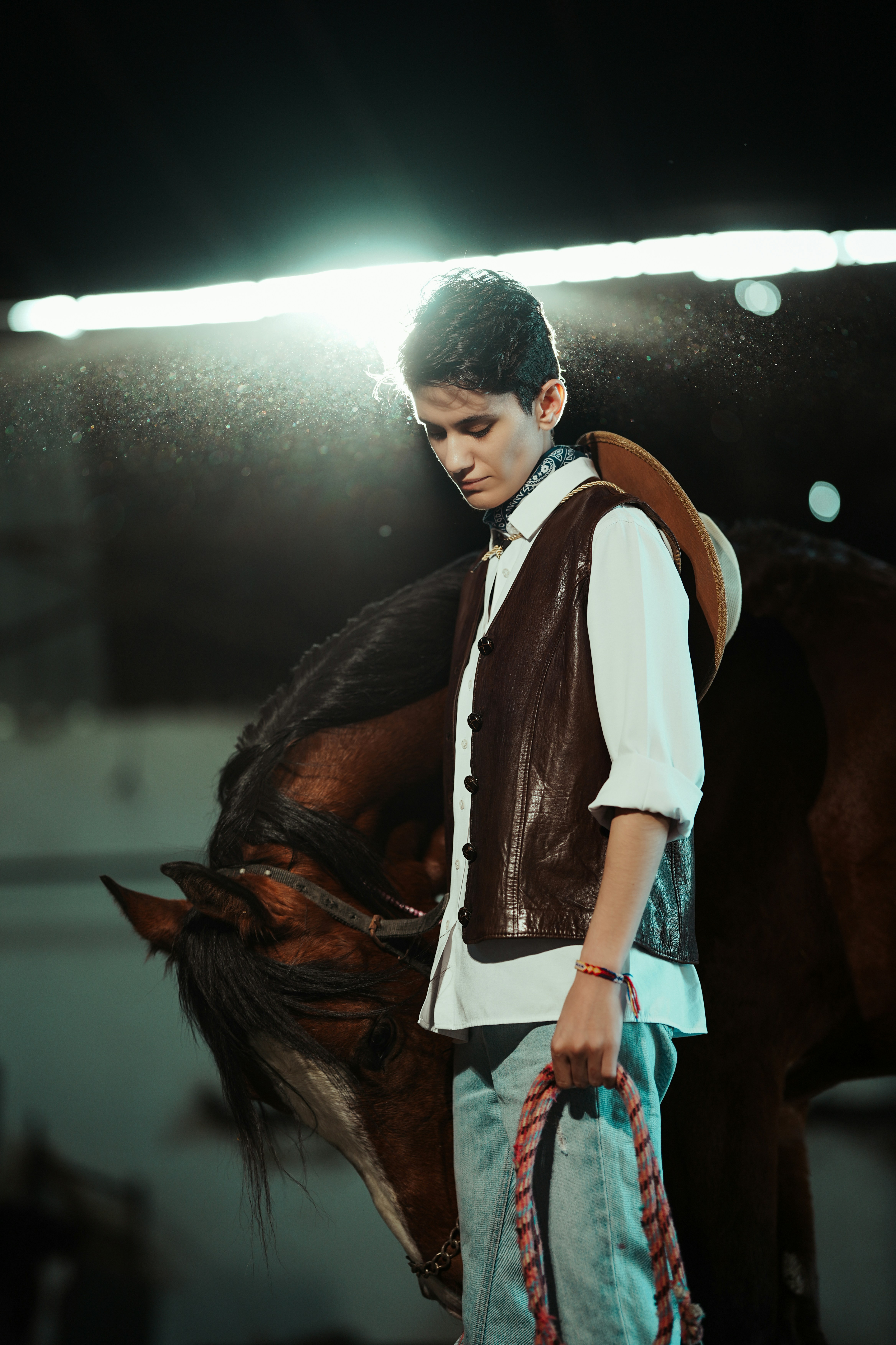 Young cowboy with horse in stable with dramatic lighting.