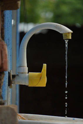 A white faucet with yellow accents drips water.