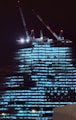 Construction cranes tower over illuminated building at night