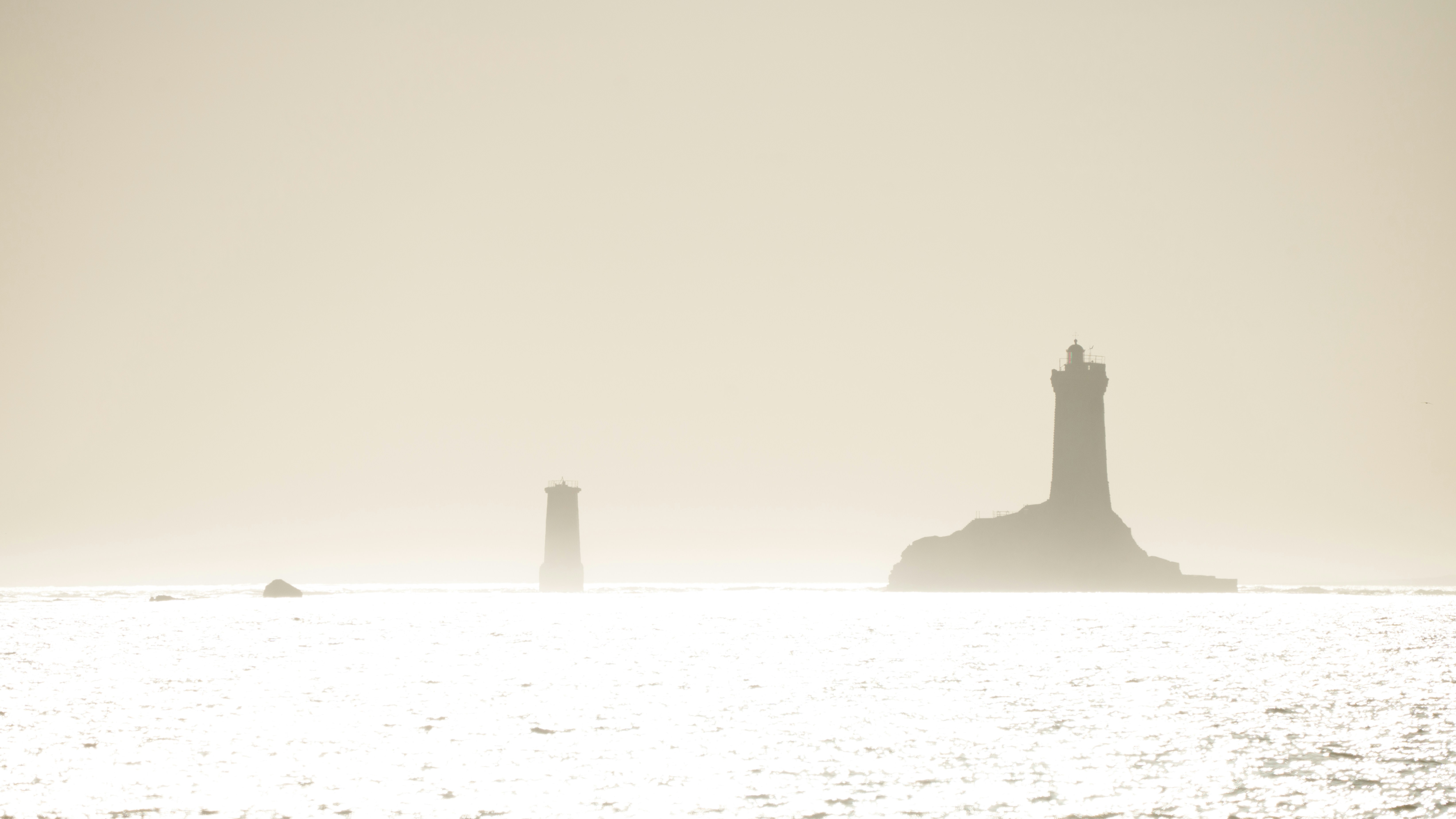Two lighthouses stand on rocky outcrops in the ocean.
