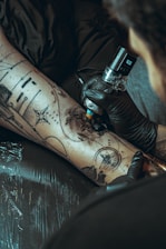 Tattoo artist applying ink to a client's leg.