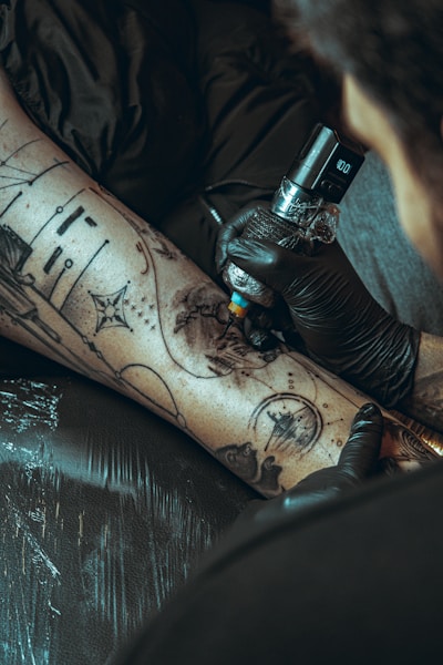 Tattoo artist applying ink to a client's leg.