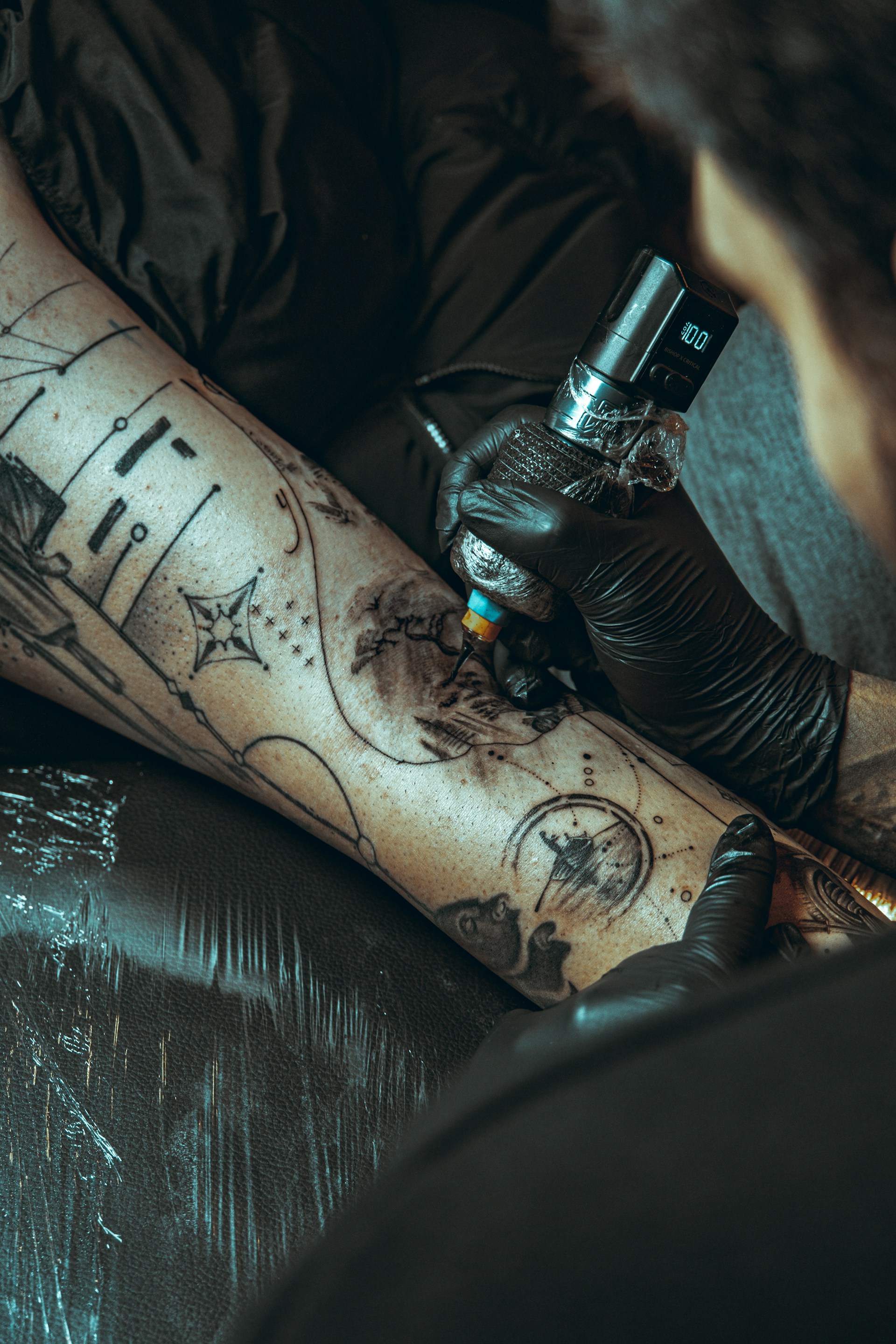 Tattoo artist applying ink to a client's leg.