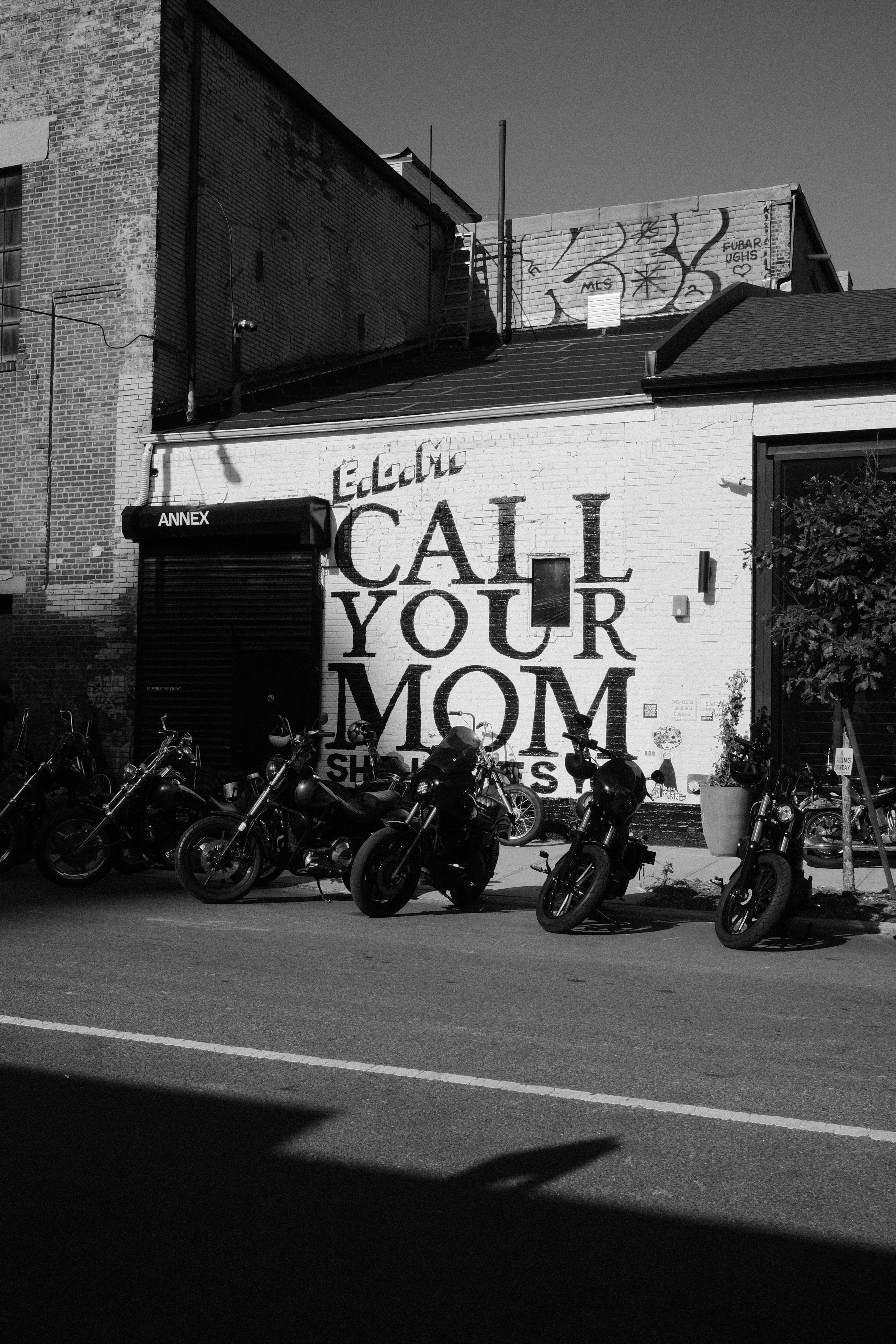 Motorcycles parked outside a building with "call your mom" graffiti.