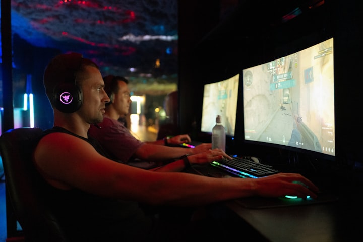 Two pro players at dual gaming workstations in a dim arena, viewed from behind
