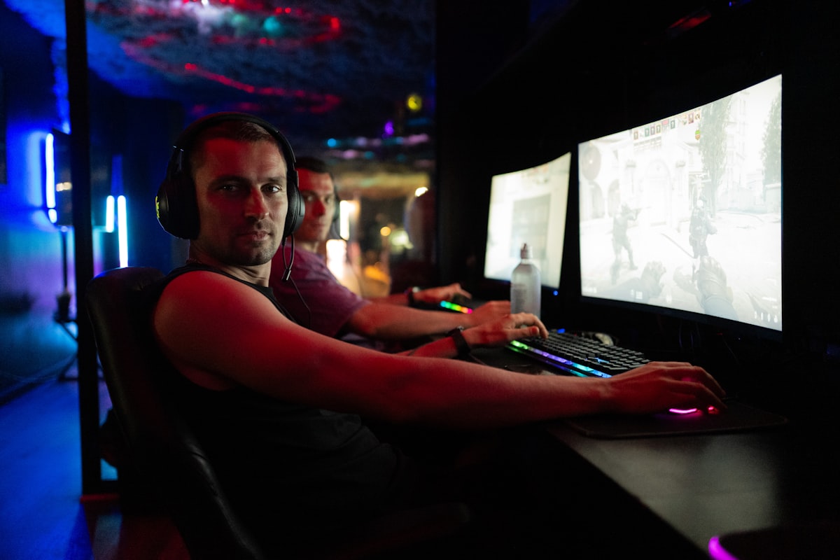 A row of gaming PCs and PlayStation booths inside a neon-lit gaming center