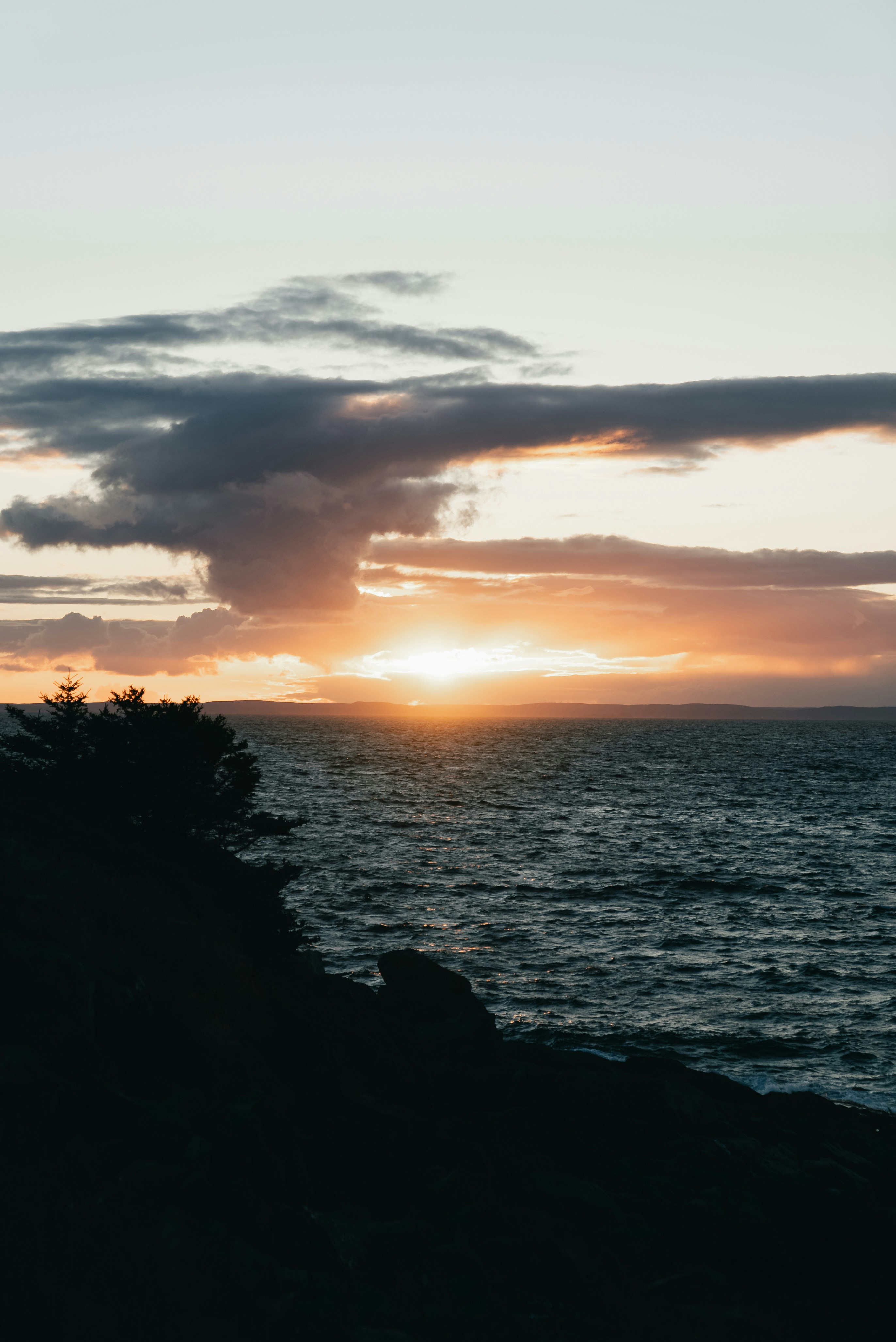 Sunset over a dark, rocky coastline and ocean.