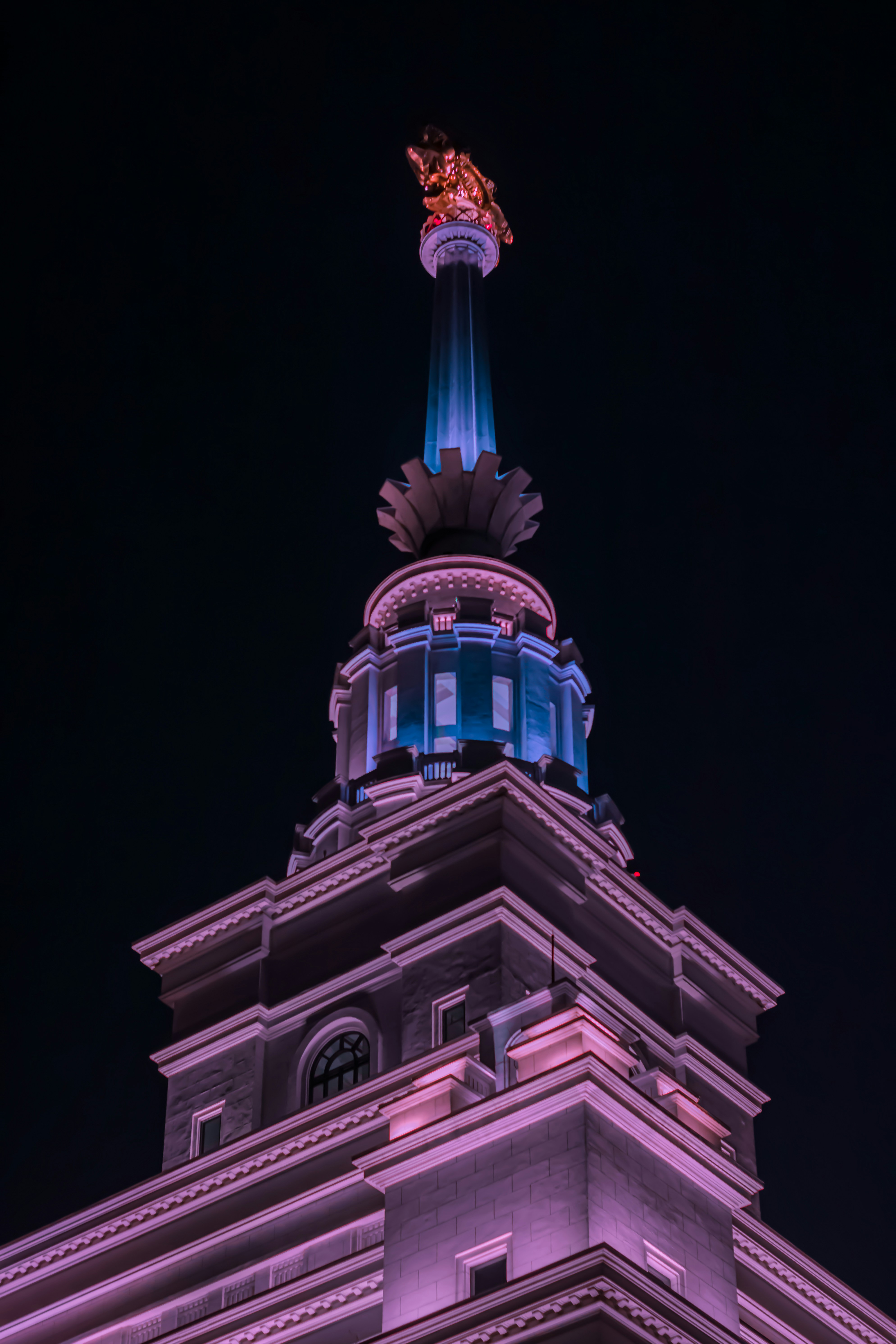 Ornate building spire illuminated with pink and blue lights.