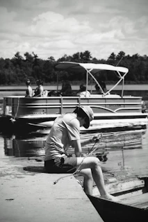 Person sitting on dock with pontoon boat behind