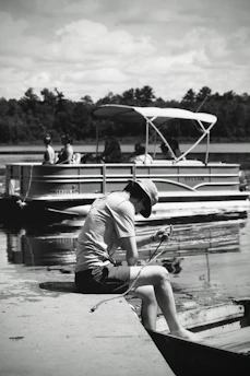 Person sitting on dock with pontoon boat behind