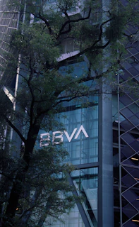Modern skyscraper with bbva logo and tree branches.