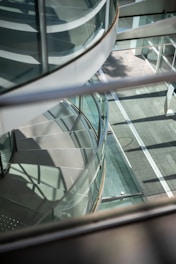 Modern spiral staircase with glass railings and shadows.