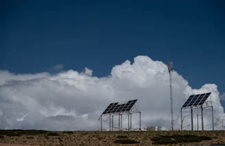 Solar panels and communication tower under a cloudy sky.