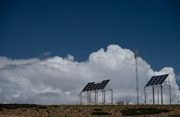Solar panels and communication tower under a cloudy sky.