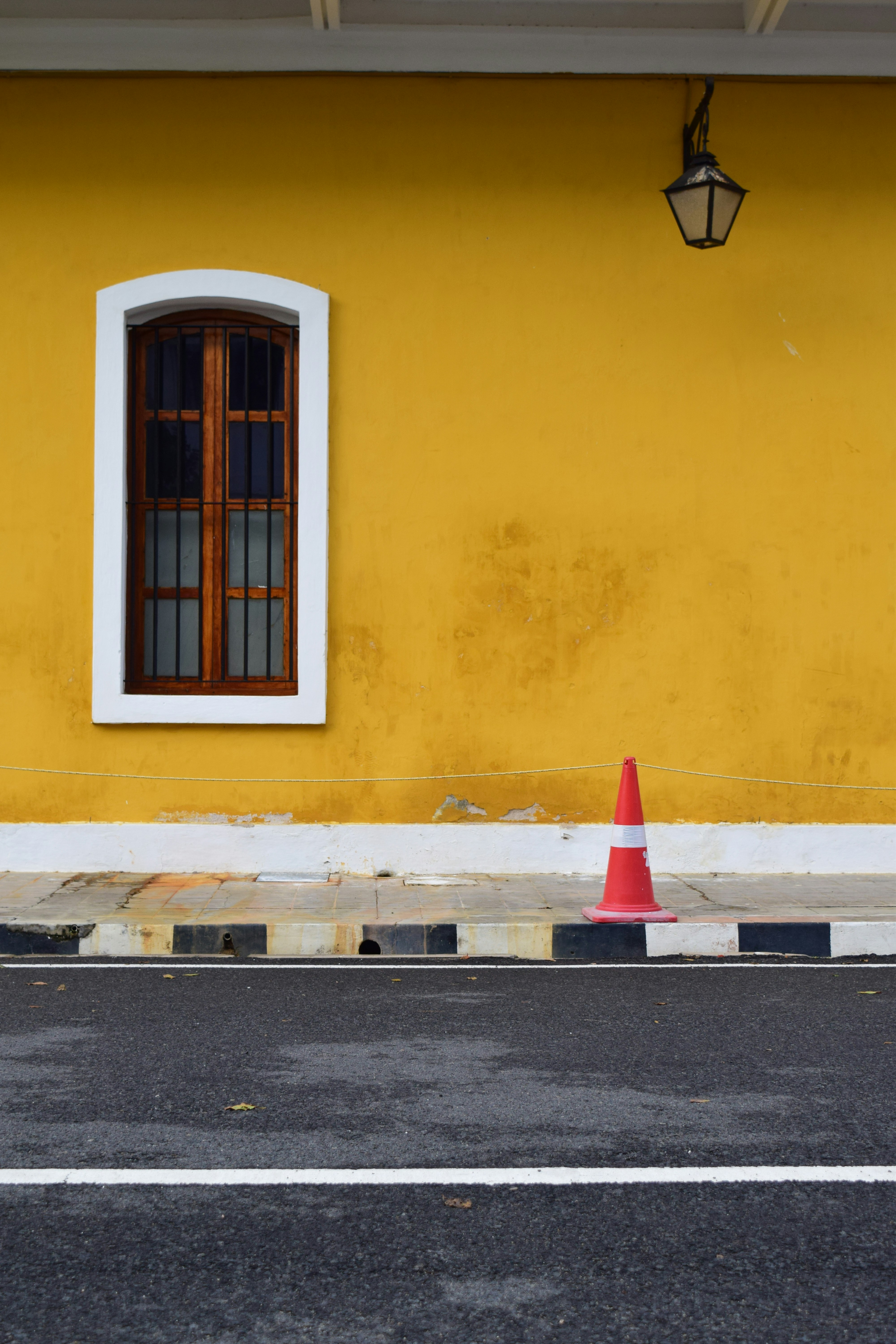 Yellow wall with window, lamppost, and traffic cone.