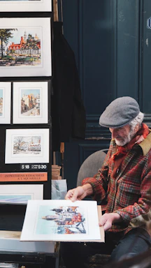 Elderly artist displays his watercolor paintings at an outdoor market.