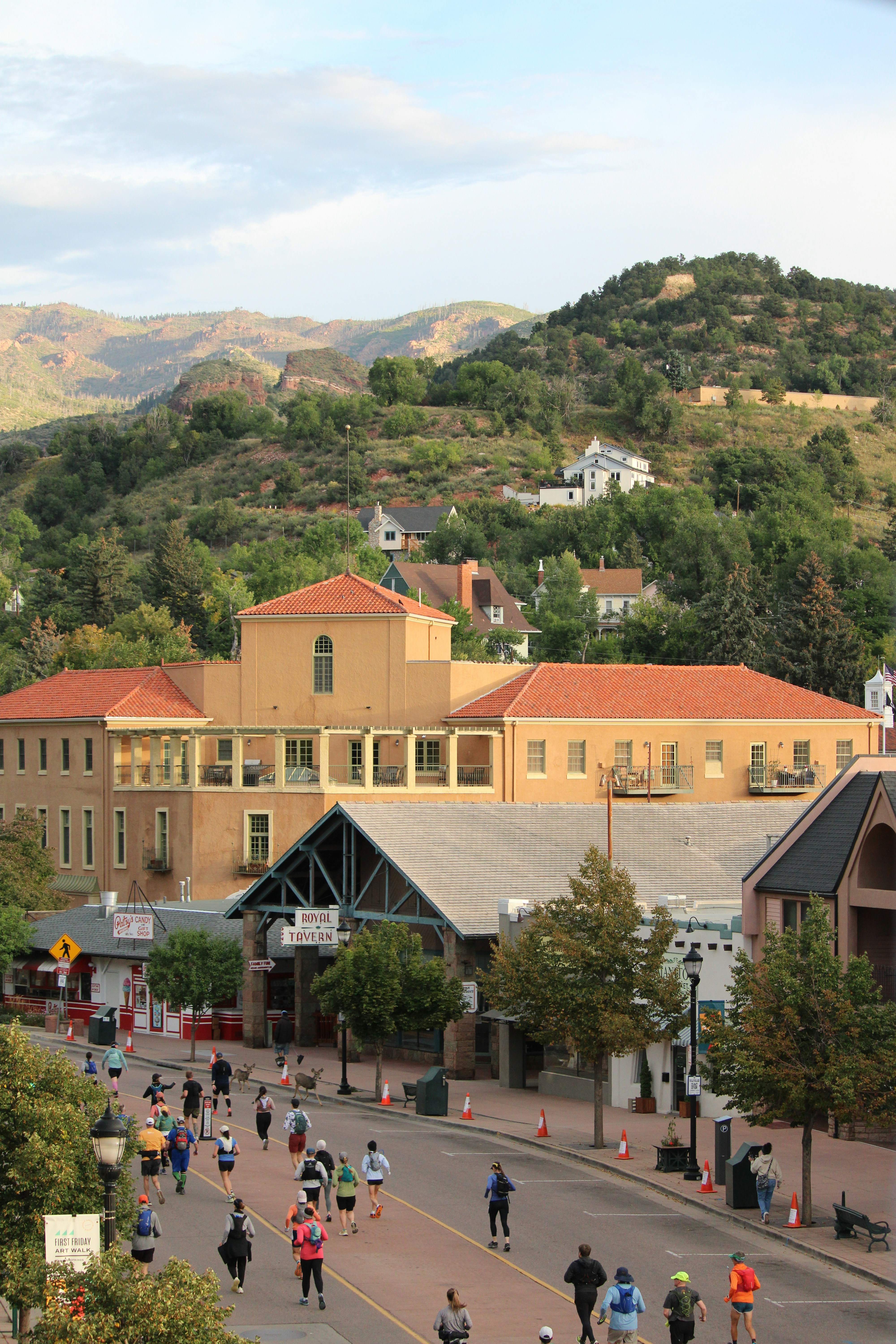 Runners race down a street with buildings and hills.