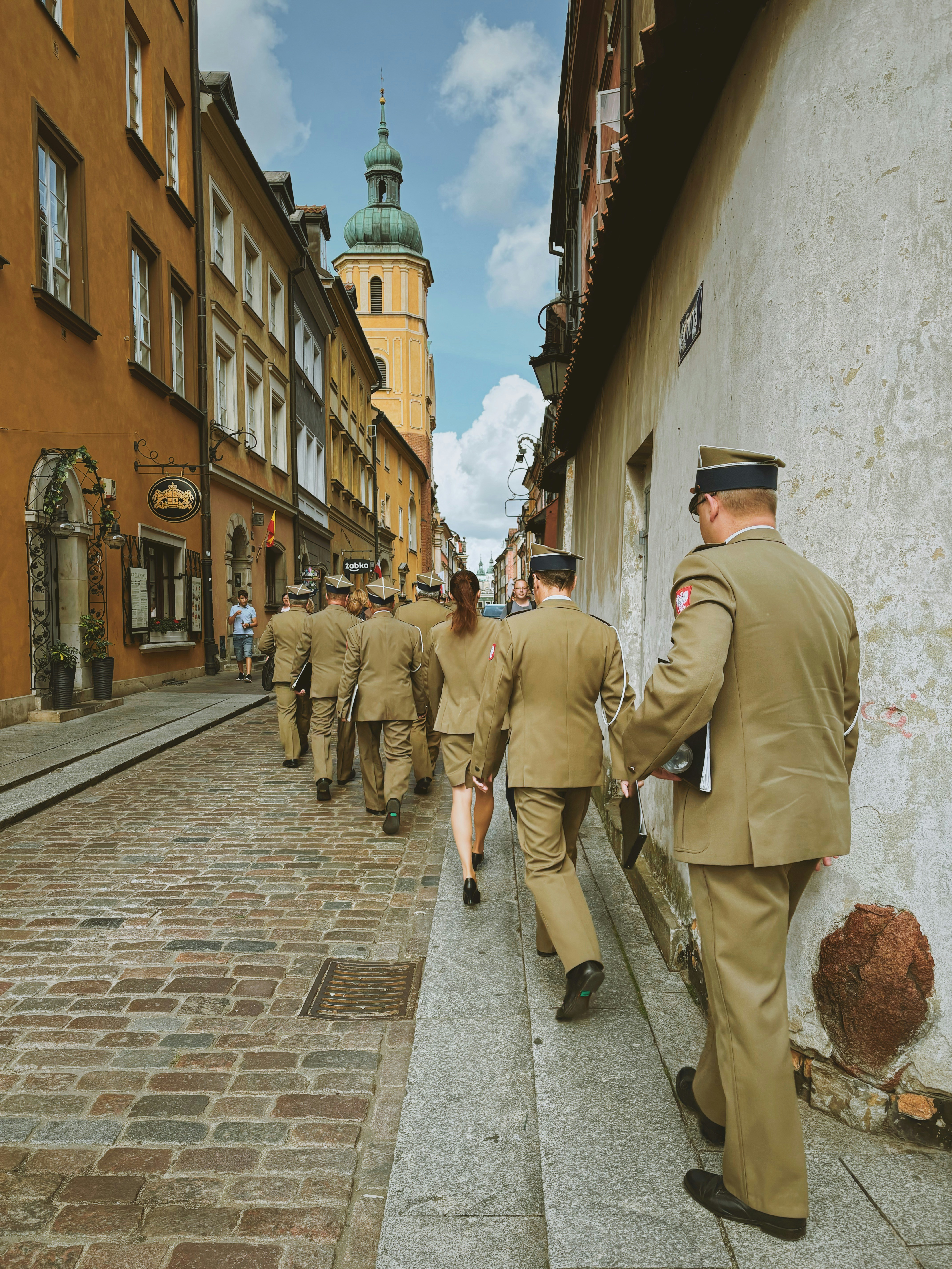 Soldiers in uniform walk down a cobblestone street.