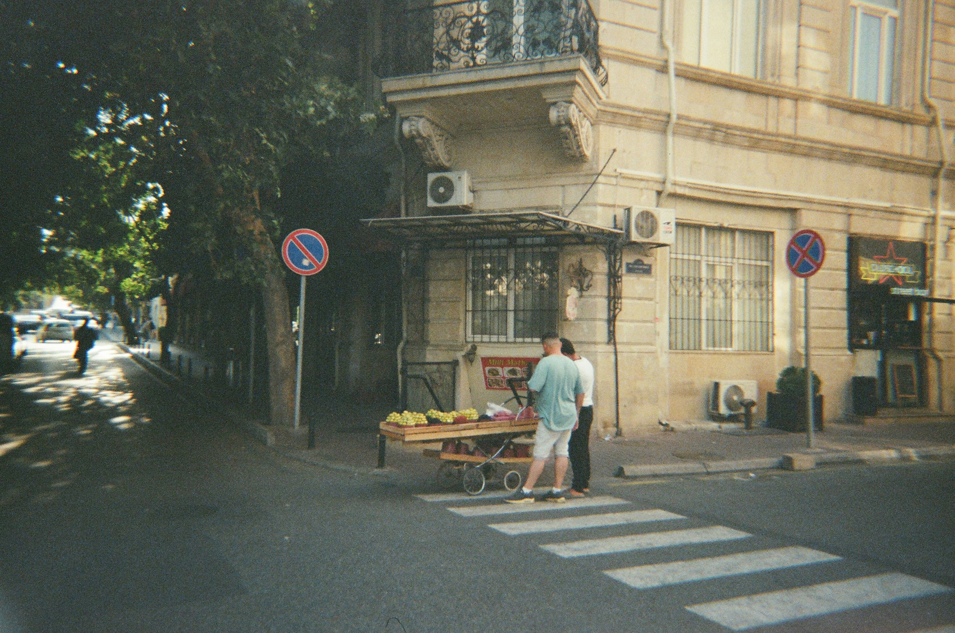 People at a fruit stand on a city street corner.