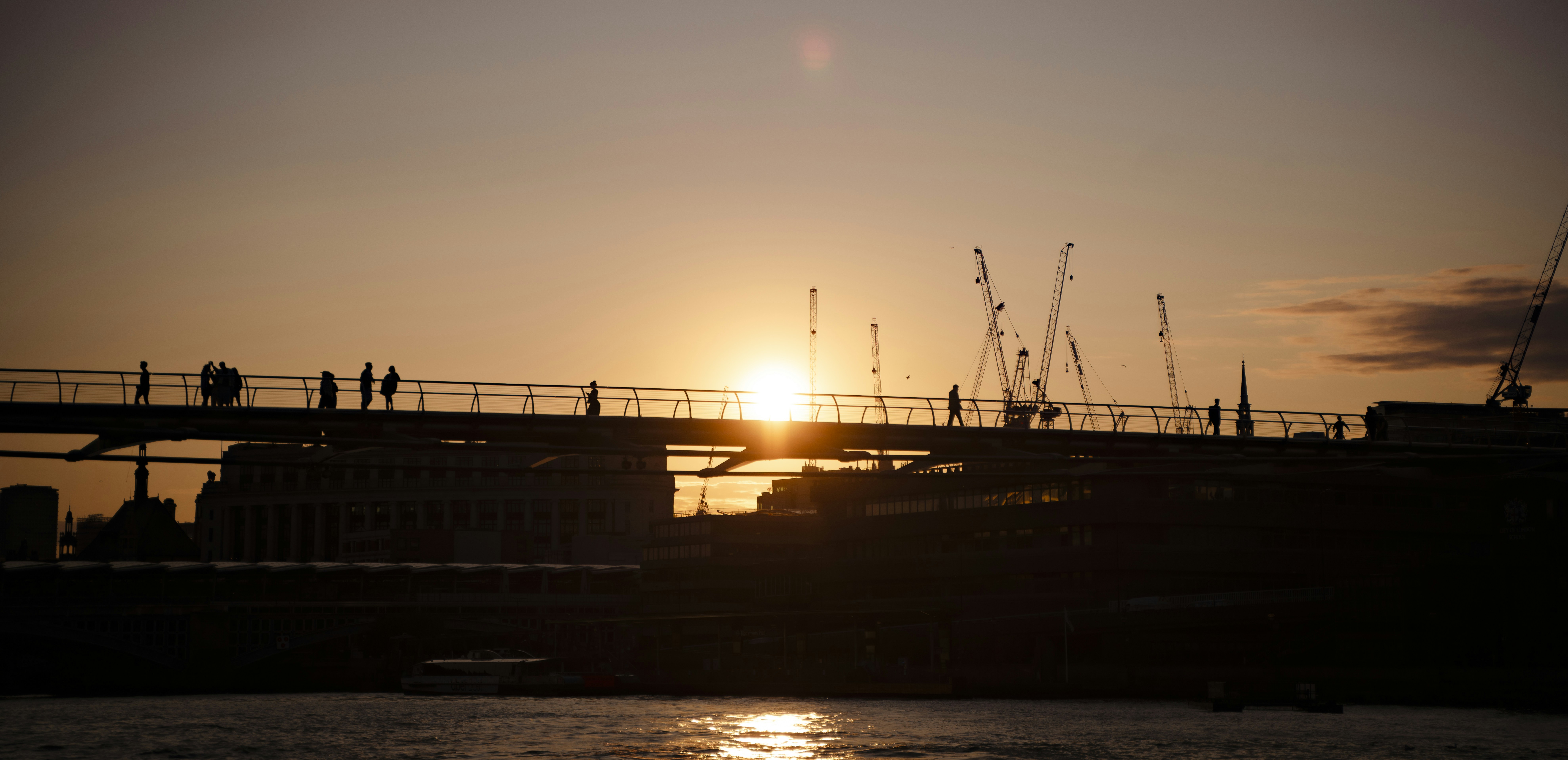 Sunset over a bridge with cranes and people.